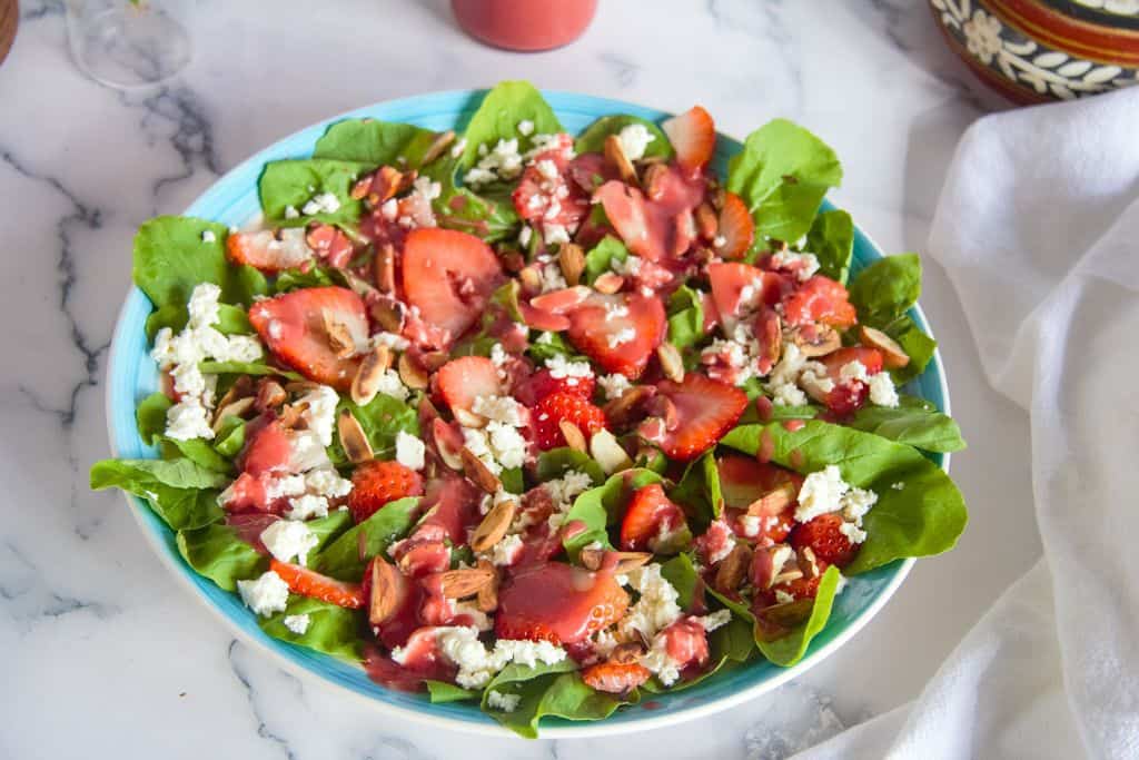 a bowl of colorful strawberries, arugula, feta and almonds