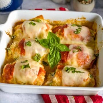 A white baking dish filled with six cheese-topped stuffed bell peppers, reminiscent of savory chicken rollatini, garnished with fresh basil leaves.