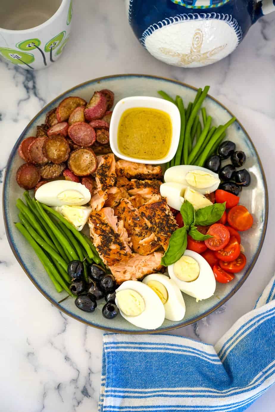 salmon, olives, tomatoes, green beans and radishes on a plate with salad dressing in a small bowl.