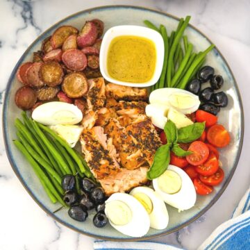 Plate of food including sliced radishes, green beans, hard-boiled eggs, olives, cherry tomatoes, grilled chicken, and a bowl of dipping sauce—perfect for a keto salmon salad.