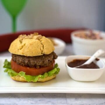 A keto turkey burger with lettuce and tomato on a plate, accompanied by a small bowl of sauce and a few other dishes in the background.