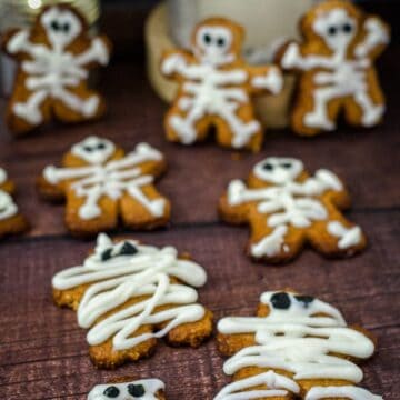 Keto Halloween gingerbread cookies decorated as skeletons and mummies with white icing, placed on a wooden surface.