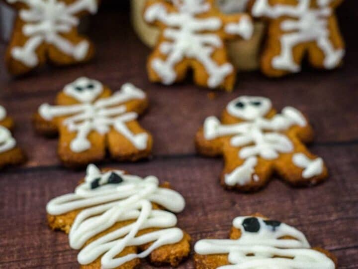 Keto Halloween gingerbread cookies decorated as skeletons and mummies with white icing, placed on a wooden surface.