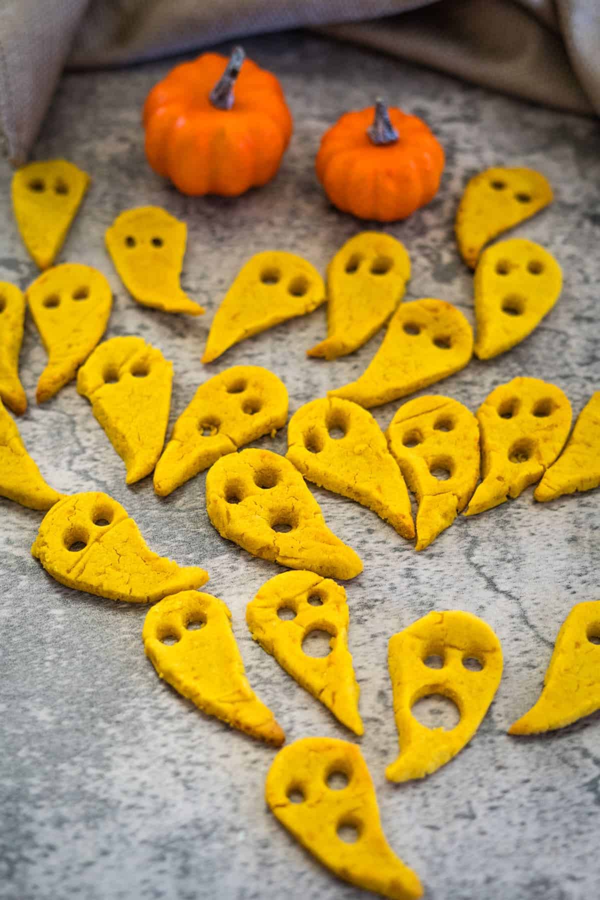 Keto ghost-shaped cookies arranged on a surface with two small decorative pumpkins in the background create a perfect Halloween treat that's both spooky and diet-friendly.