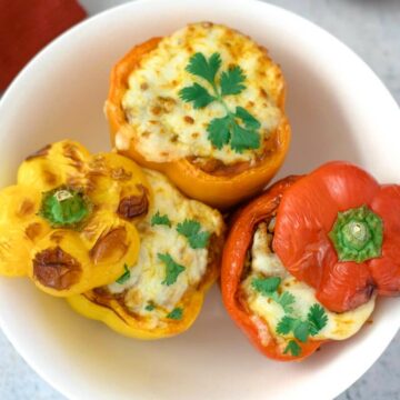 A white plate holds three air fryer stuffed peppers—two orange, one red—topped with melted cheese and garnished with cilantro.