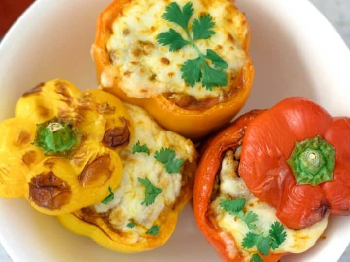 A white plate holds three air fryer stuffed peppers—two orange, one red—topped with melted cheese and garnished with cilantro.