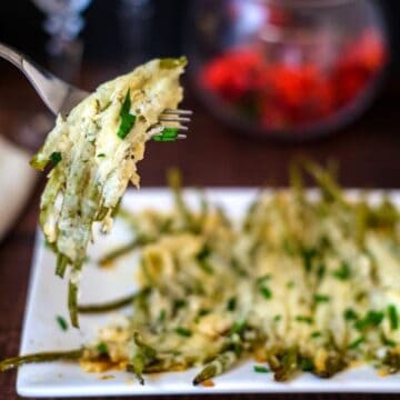 A fork lifts a portion of cheesy keto green bean casserole from a white plate.