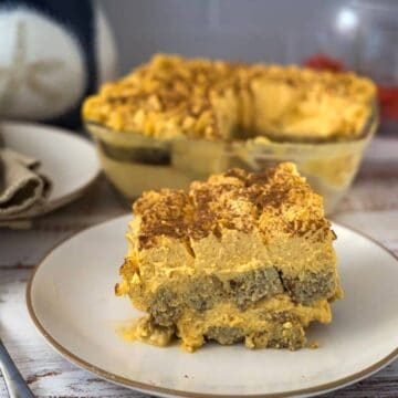 A plate containing a slice of layered pumpkin tiramisu with crumbled topping, in front of a glass dish with more of the same dessert.