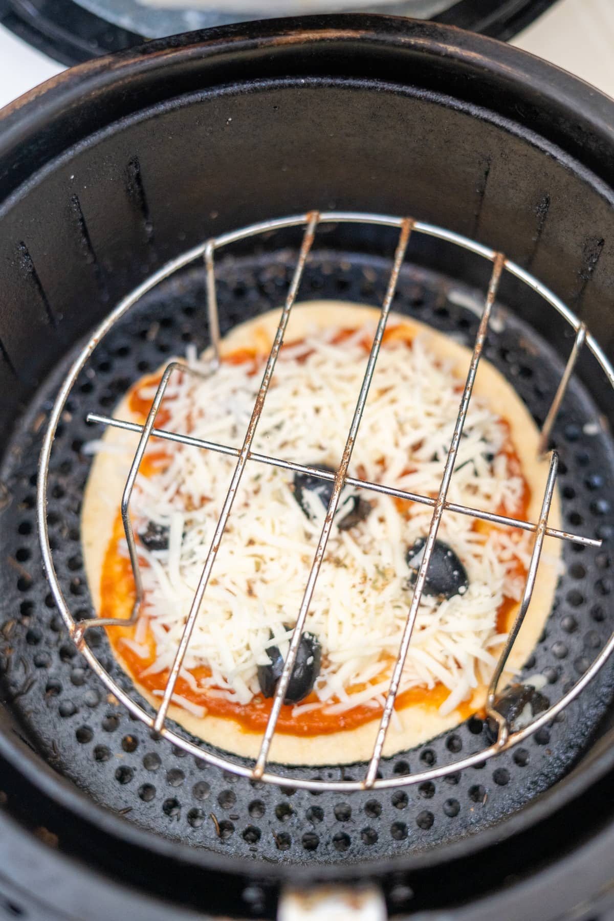 A tortilla pizza is being cooked in an air fryer.