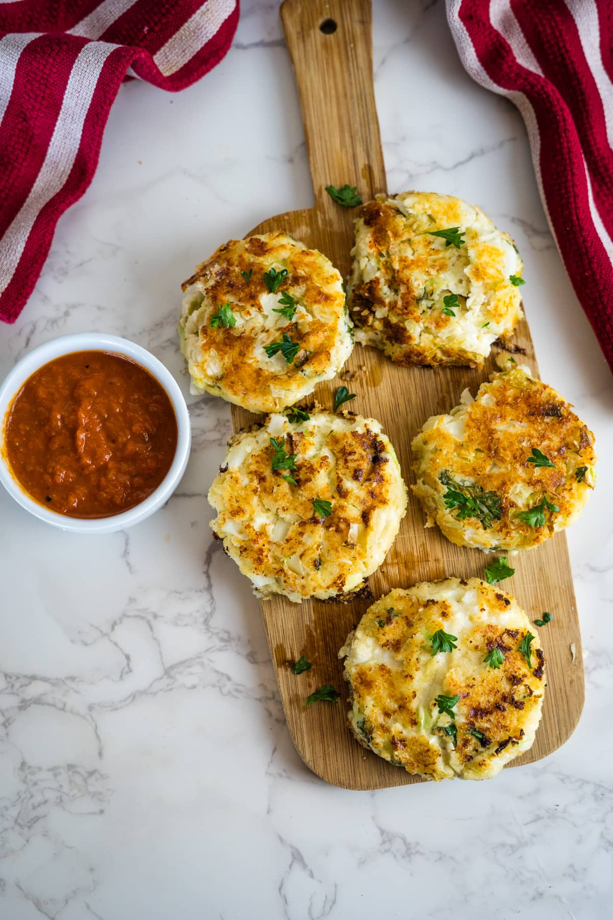 Cheesy cauliflower cabbage fritters on a cutting board with dipping sauce.