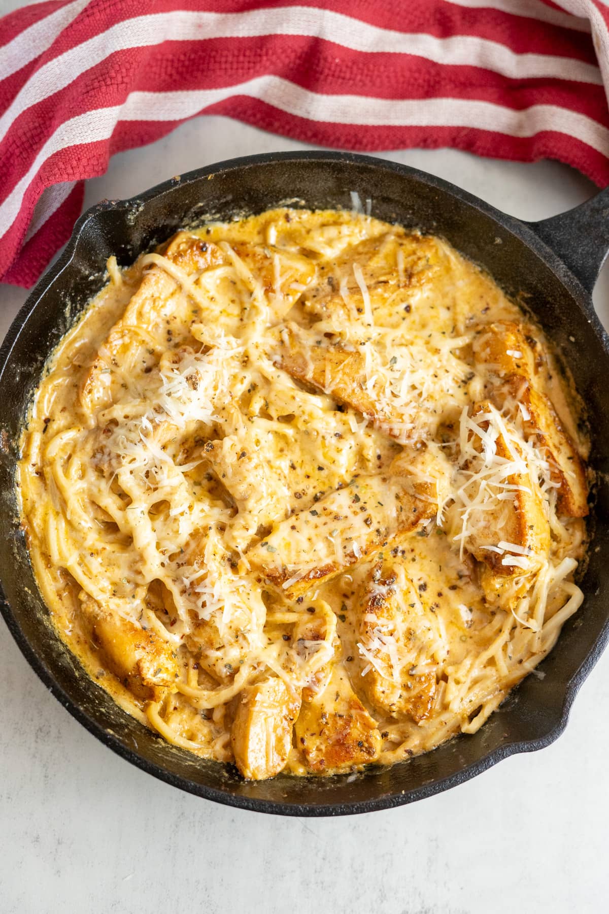 Cheesy chicken pasta in a skillet on a red and white striped tablecloth.