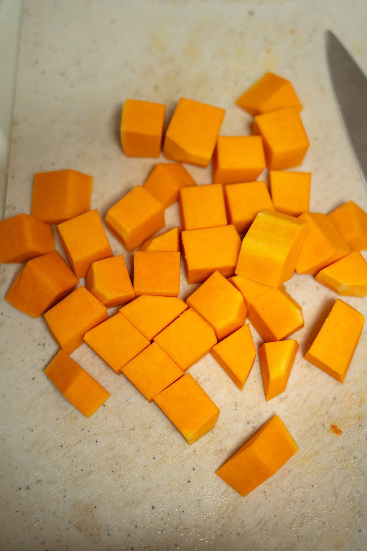 A knife on a cutting board next to a pile of orange cubes.