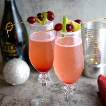 Two glasses of champagne with cranberries and limes.