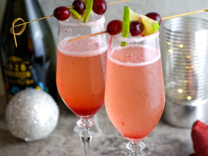 Two glasses of champagne with cranberries and limes.