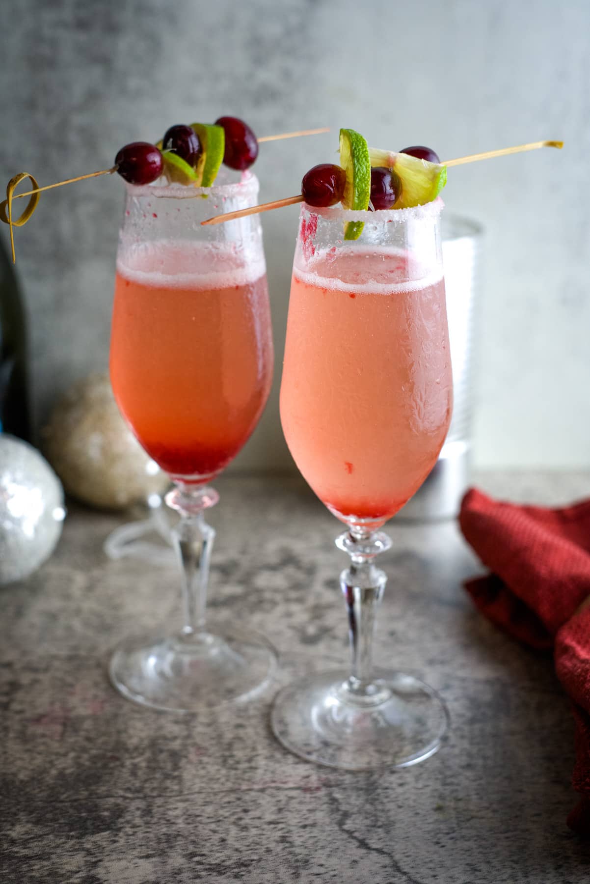 Two glasses of cranberry cocktail served with garnishes, resembling a cranberry mimosa.
