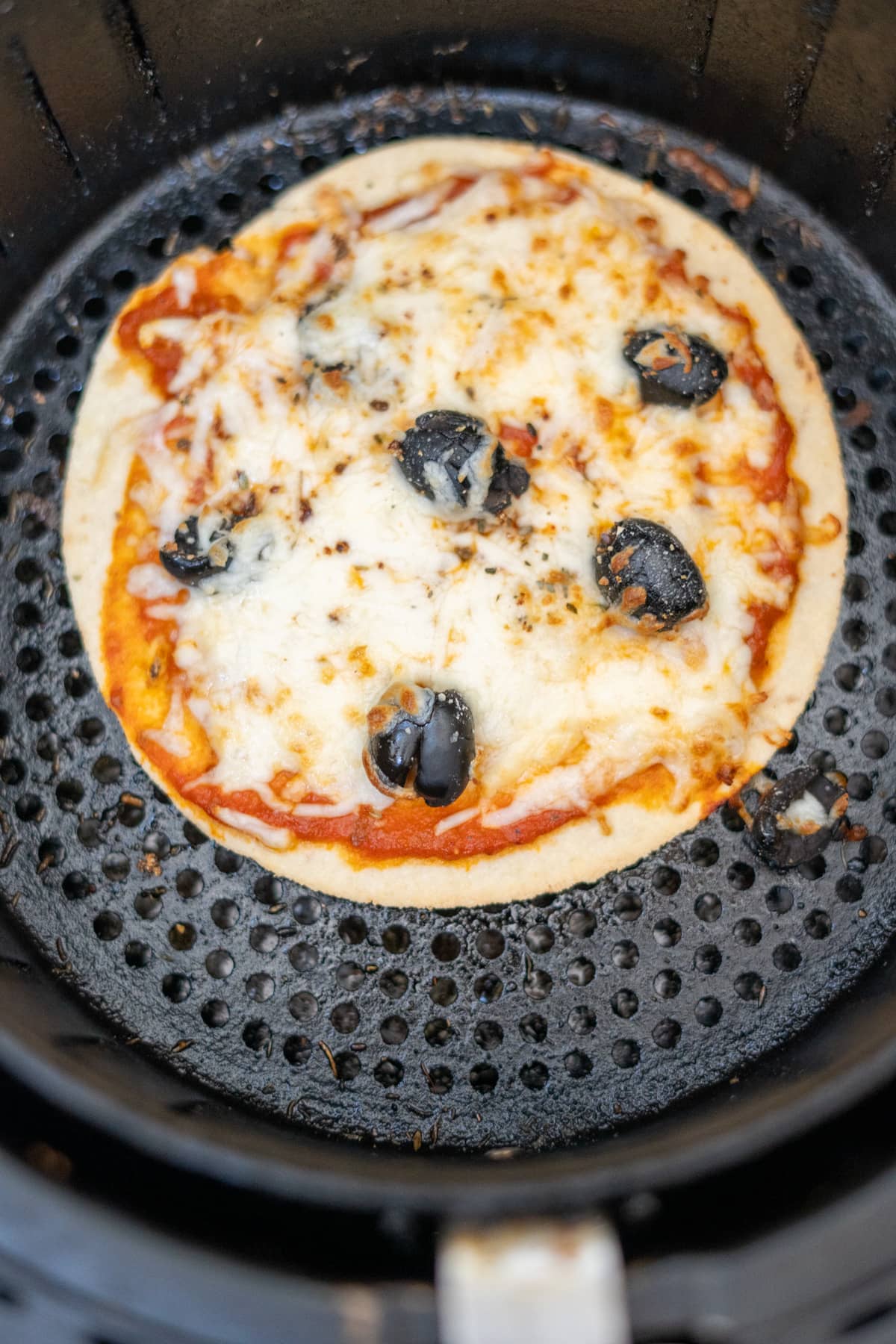 A tortilla pizza is being cooked in an air fryer.