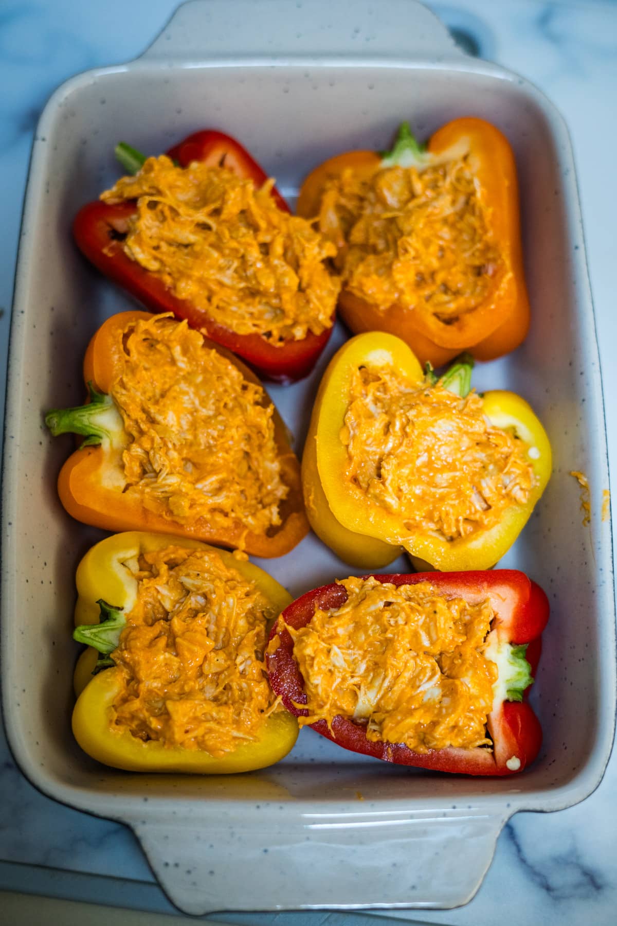 Buffalo chicken stuffed peppers in a white baking dish.