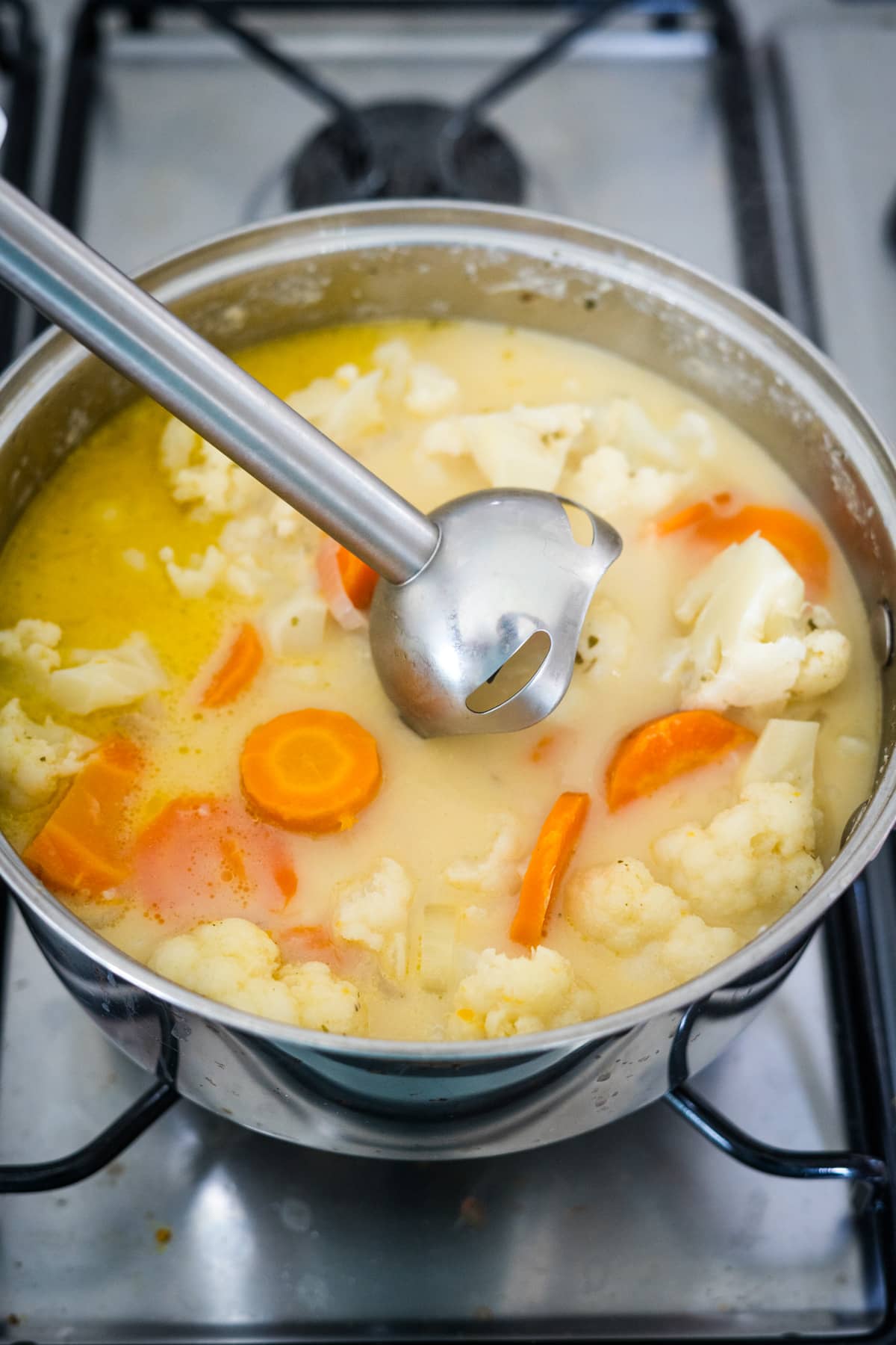 A pot of soup with carrots and cauliflower on the stove.