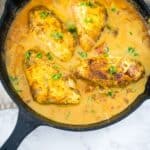 Chicken breasts in a cast iron skillet with sauce.