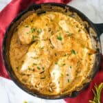 A cast iron skillet with chicken in a cream sauce.