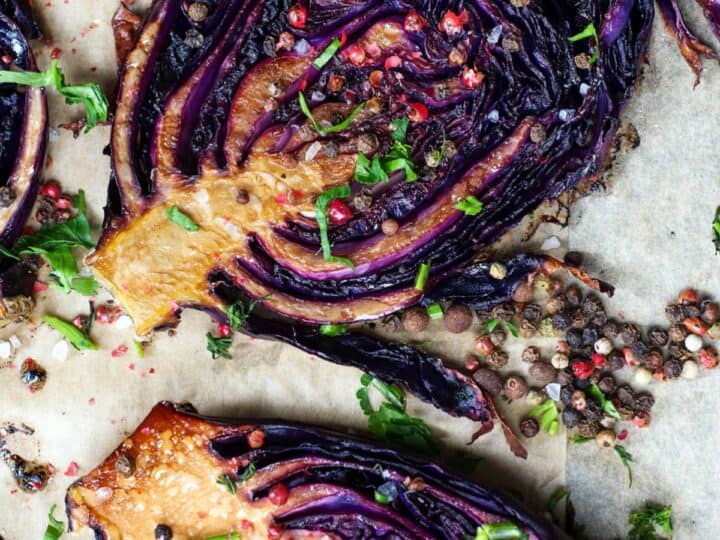 Roasted purple cabbage with spices and herbs on a baking sheet.