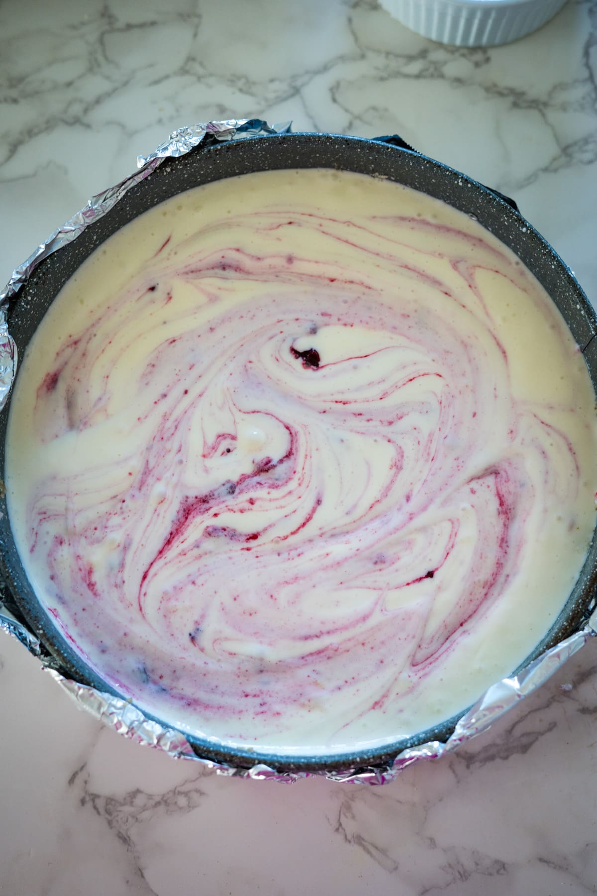 A cranberry cheesecake in a pan on a marble counter.