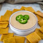 A bowl of jalapeno dip with crackers around it.