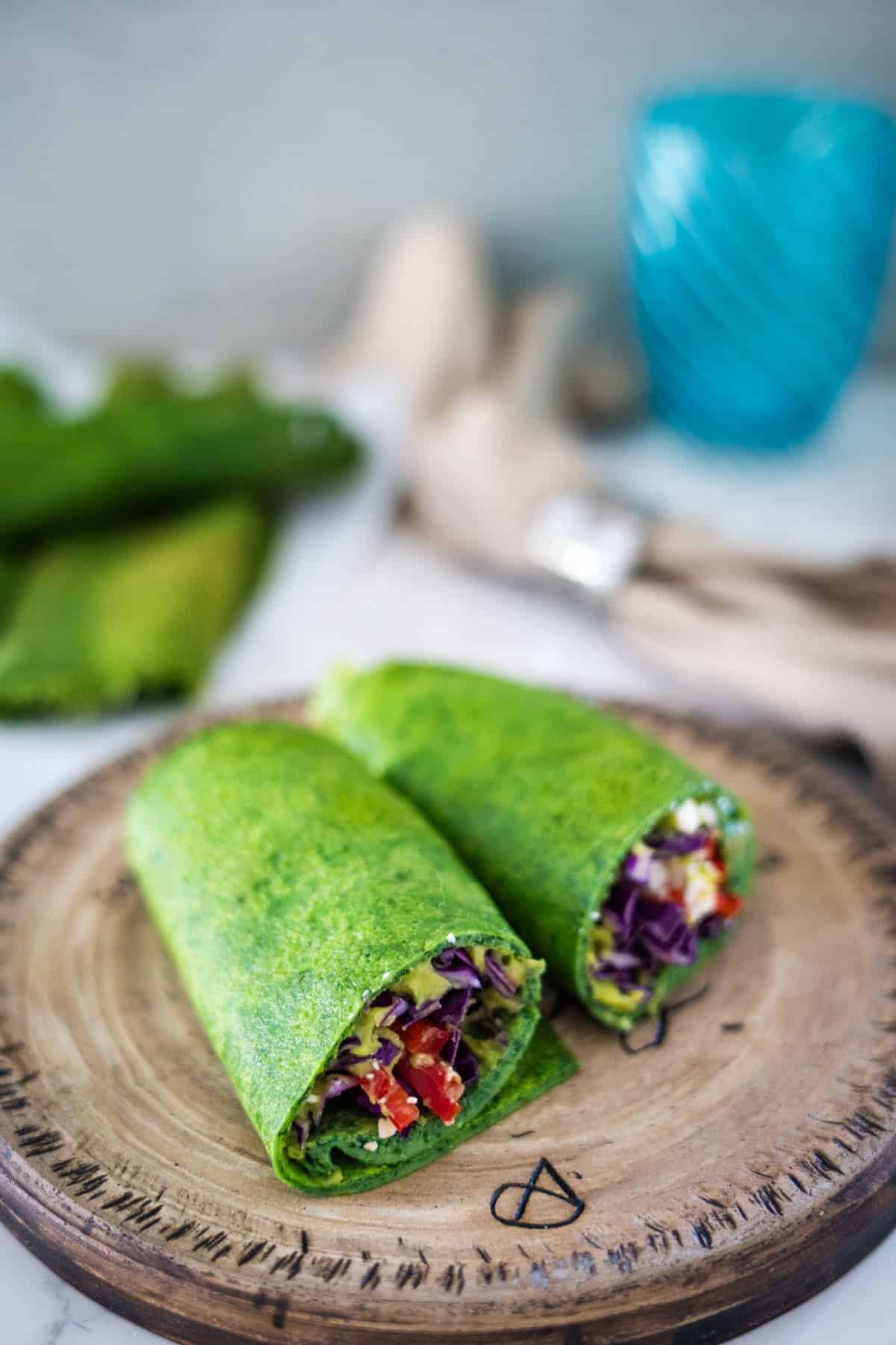 Two spinach wraps on a wooden plate.