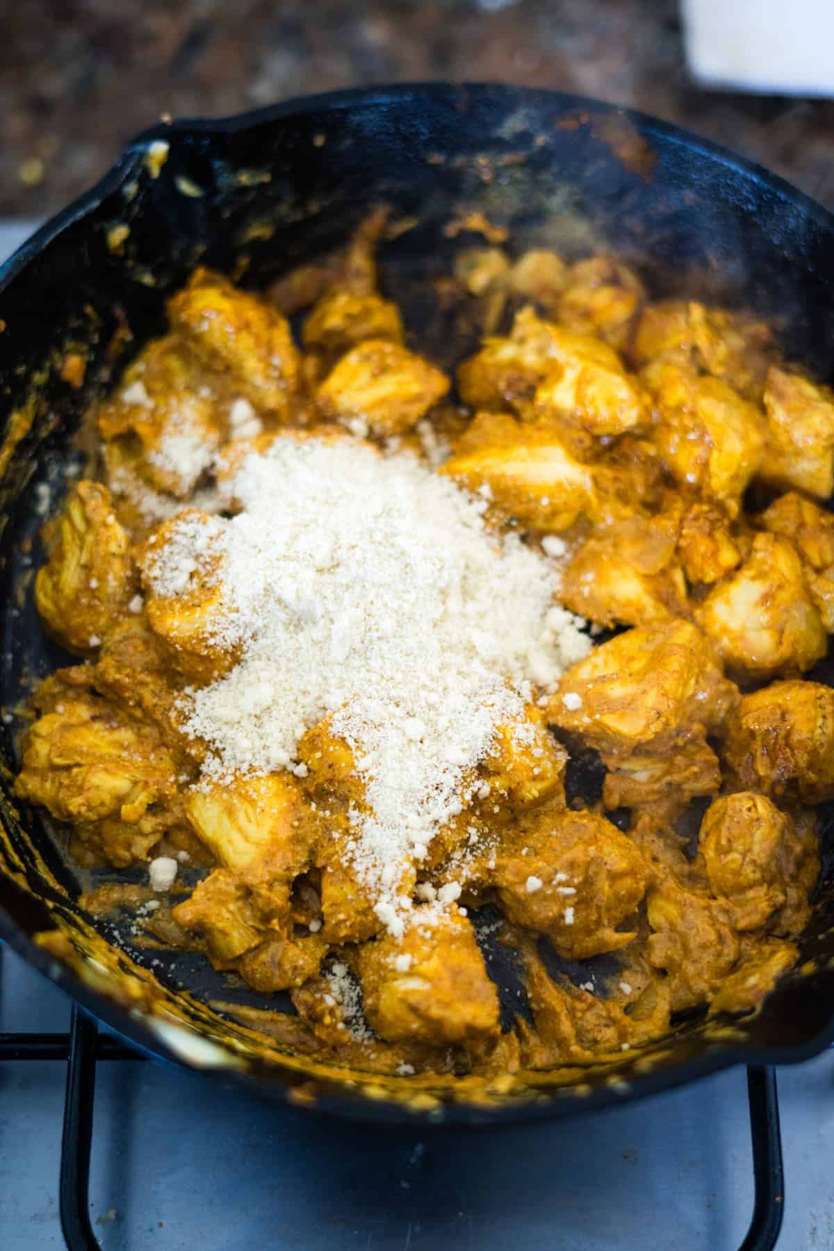 A chicken pasanda sizzling in a frying pan on a stove top.