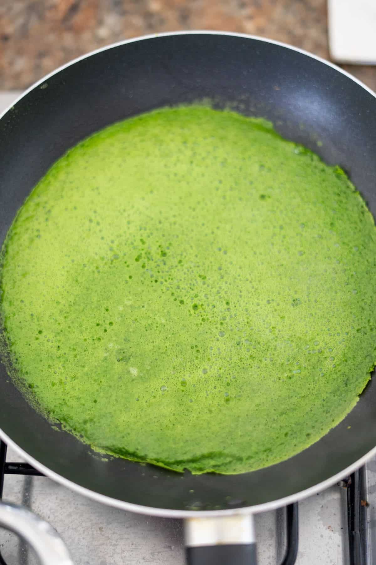 A frying pan with a green spinach egg wrap in it.