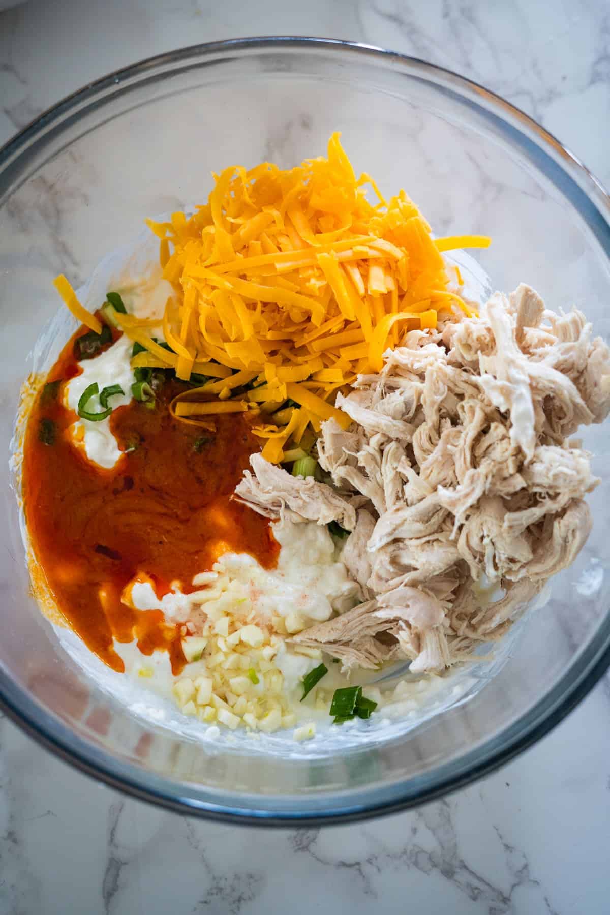 The ingredients for a buffalo chicken taco salad in a glass bowl.
