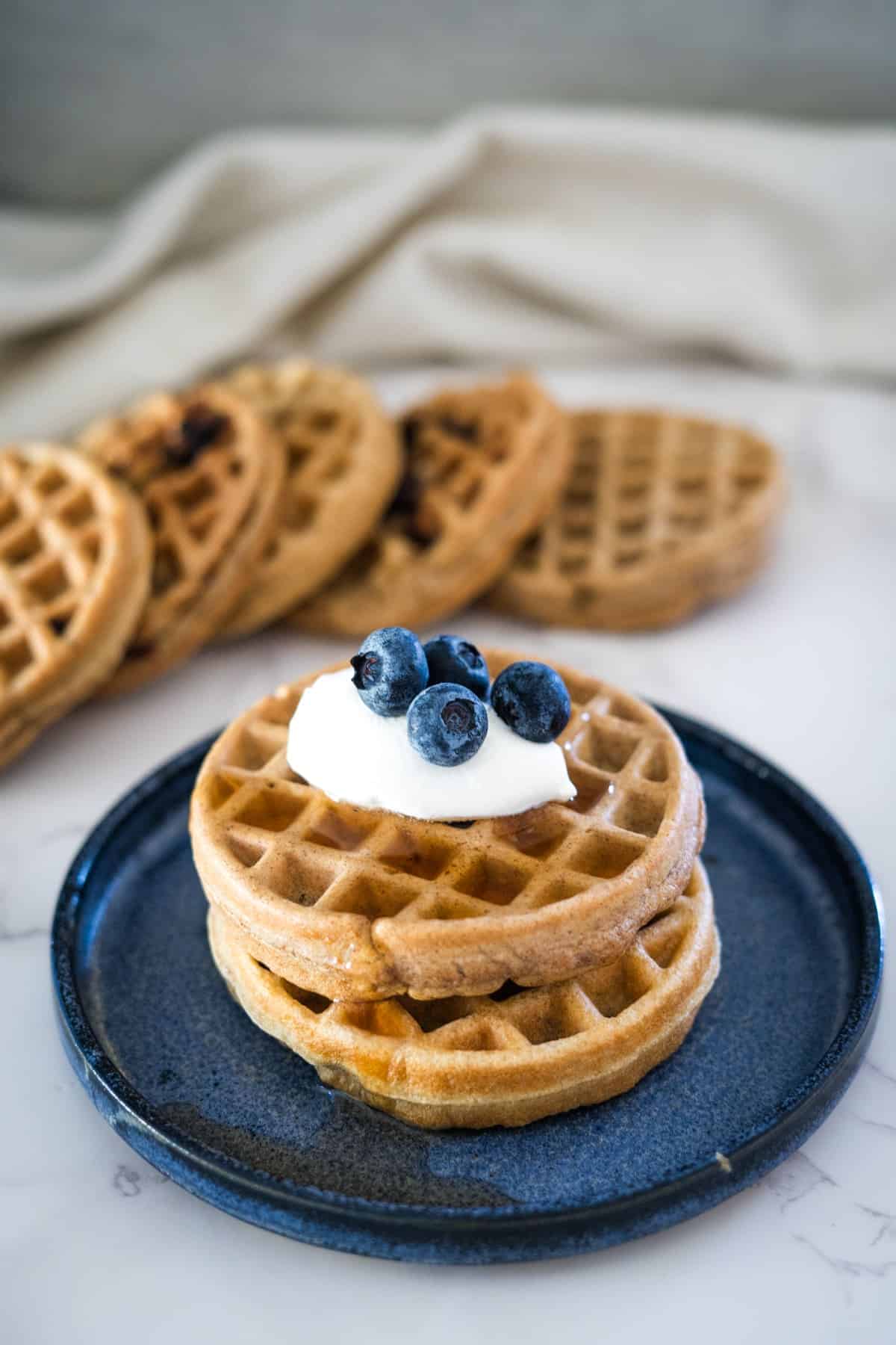 Peanut butter waffles with blueberries and whipped cream on a plate.