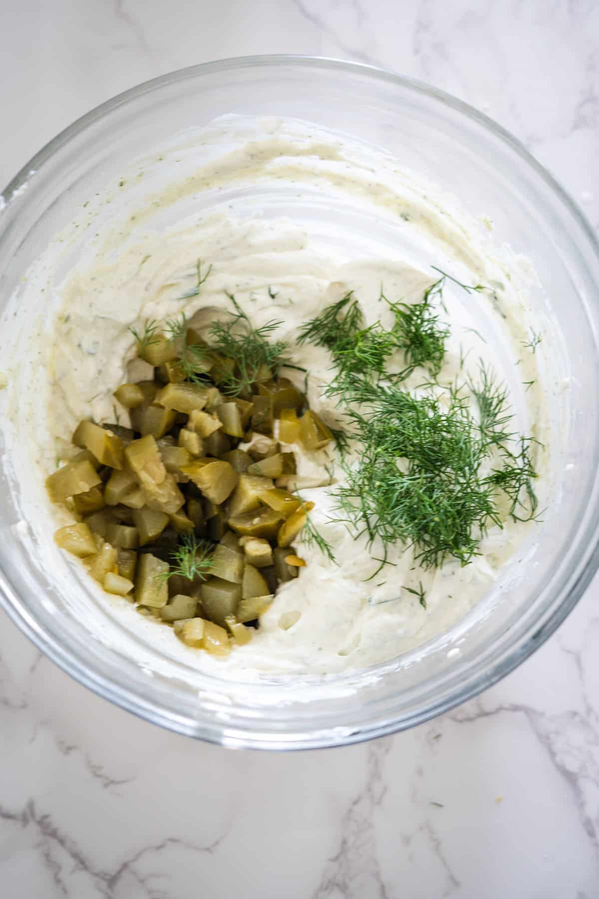 A bowl of dill dip with cucumbers and pickles, perfect for dipping fried pickles.