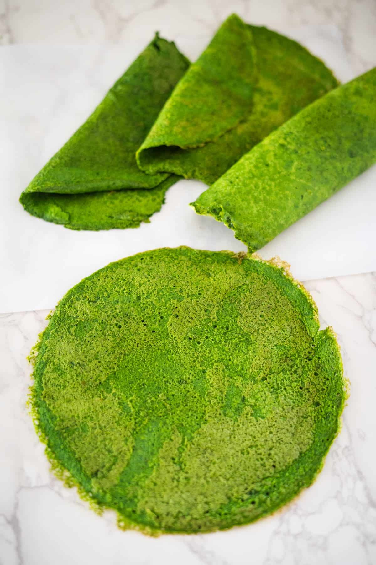 A plate of green spinach crepes on a white surface.