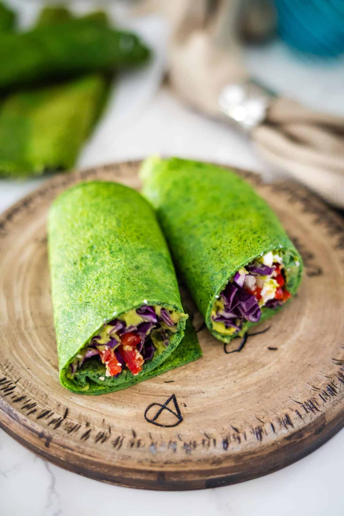 Two spinach wraps on a wooden cutting board.