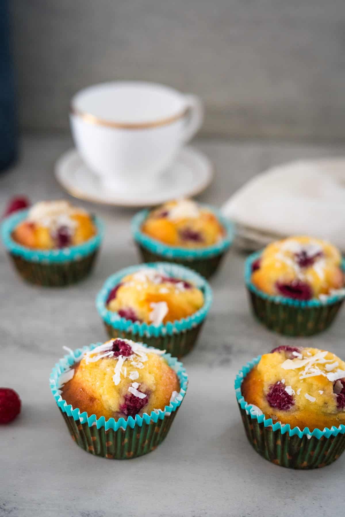 A group of keto raspberry muffins on a table next to a cup of coffee.