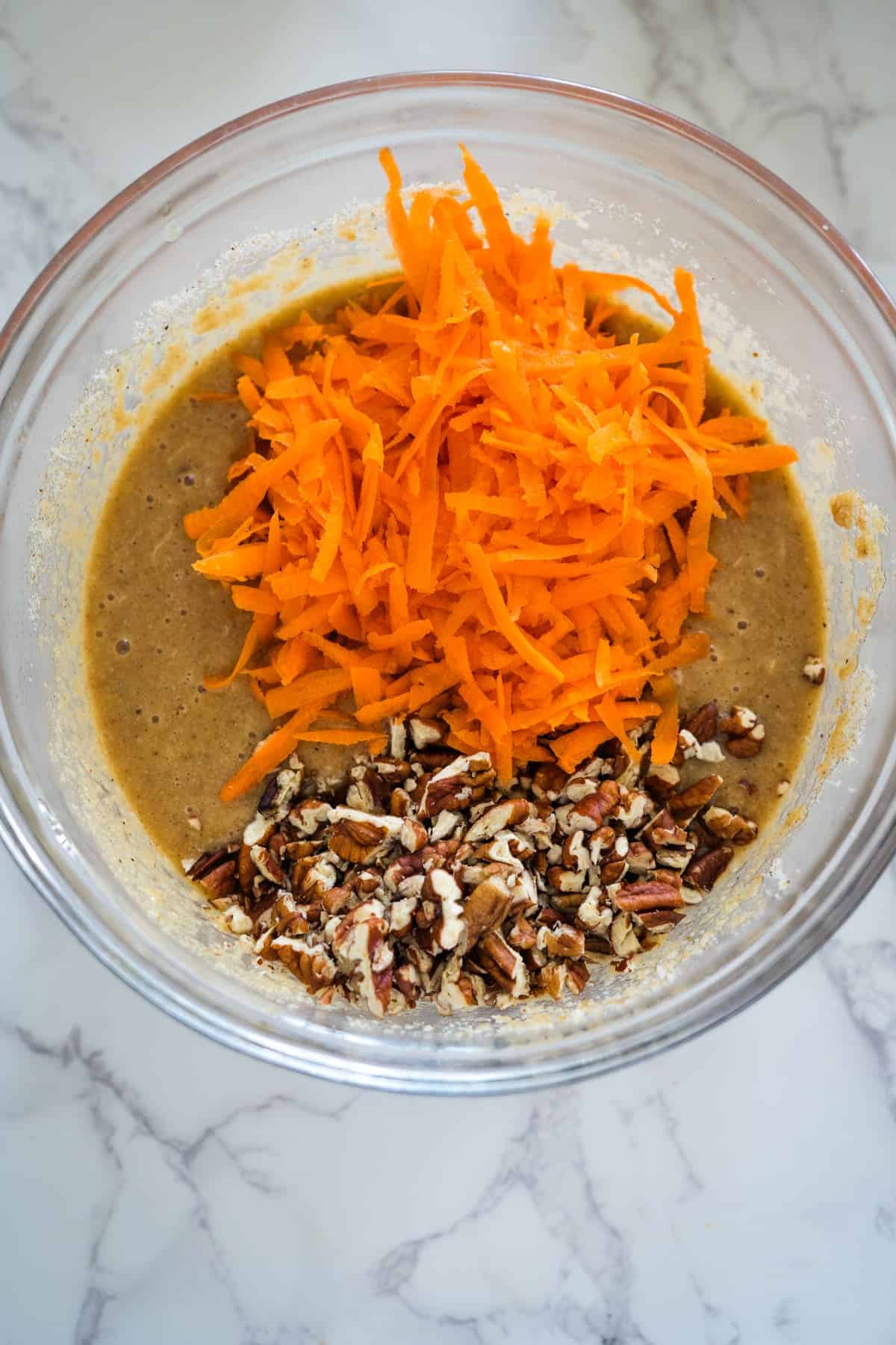 A bowl of keto batter with shredded carrots and chopped pecans ready for mixing.
