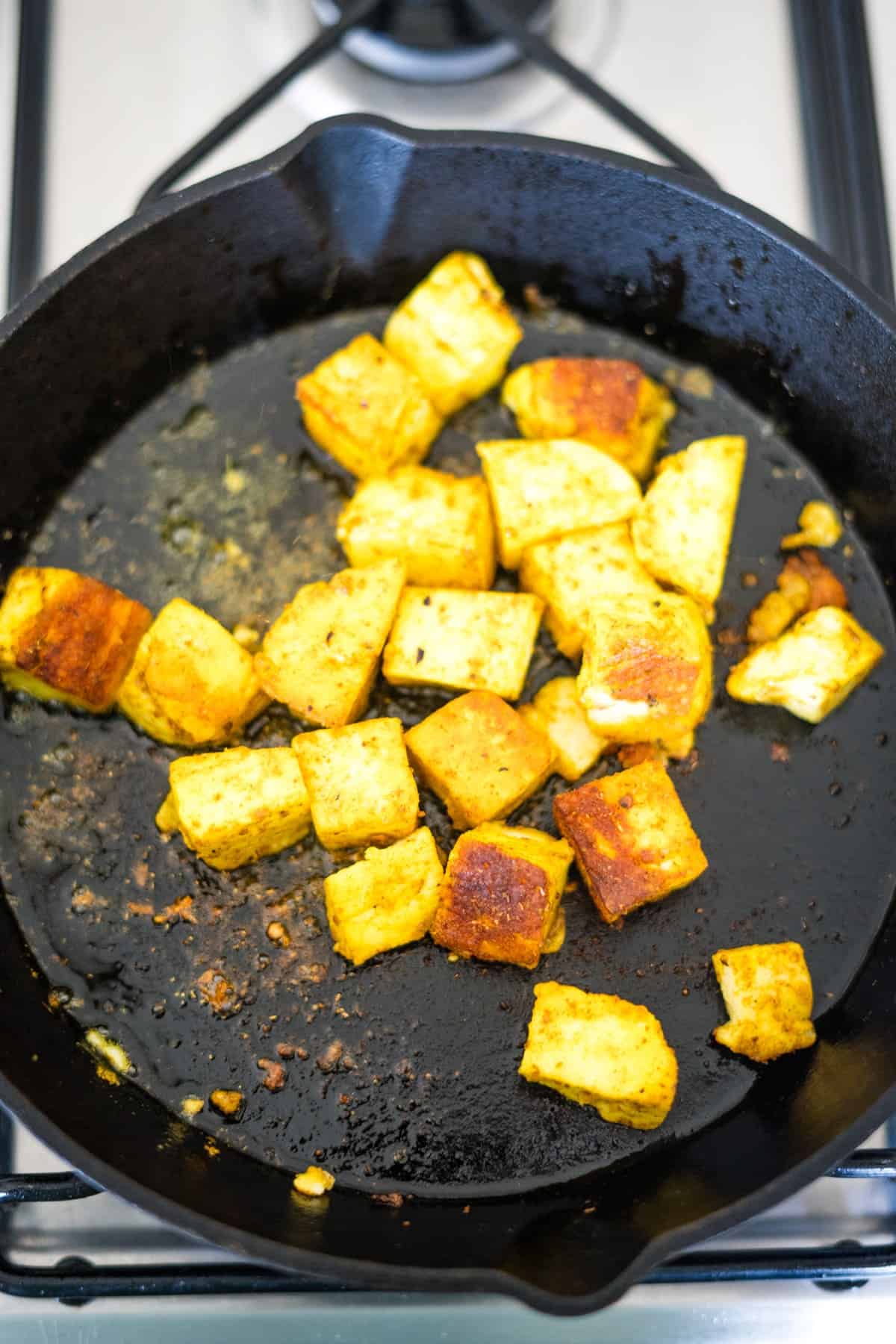 Cubed halloumi being pan-fried in a cast iron skillet on a stove.