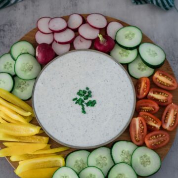 A bowl of dip surrounded by a variety of sliced vegetables on a wooden platter.