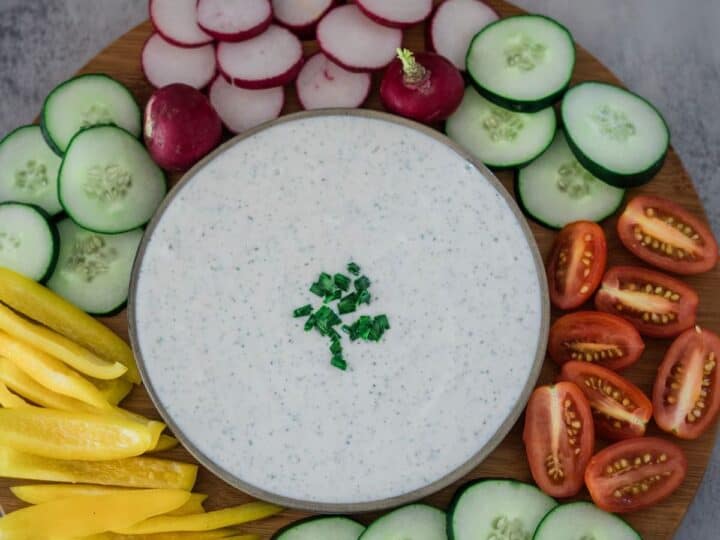 A bowl of dip surrounded by a variety of sliced vegetables on a wooden platter.