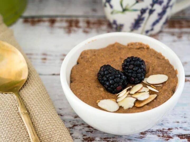 A bowl of almond-topped oatmeal garnished with blackberries, accompanied by a spoon on a cloth napkin.