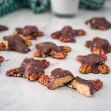 Chocolate-dipped turtle cookies with pecan halves on a countertop.