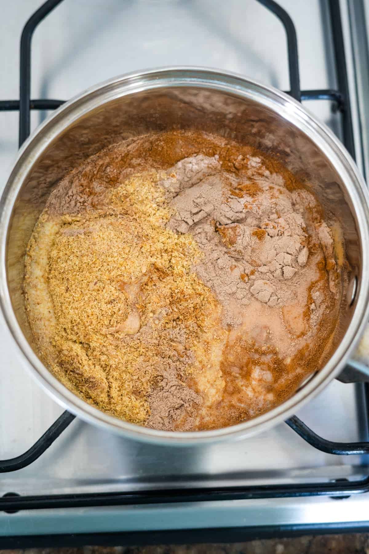 A pot on a stove containing a mixture of spices, liquids, and flaxseed, possibly at the beginning stages of cooking porridge.