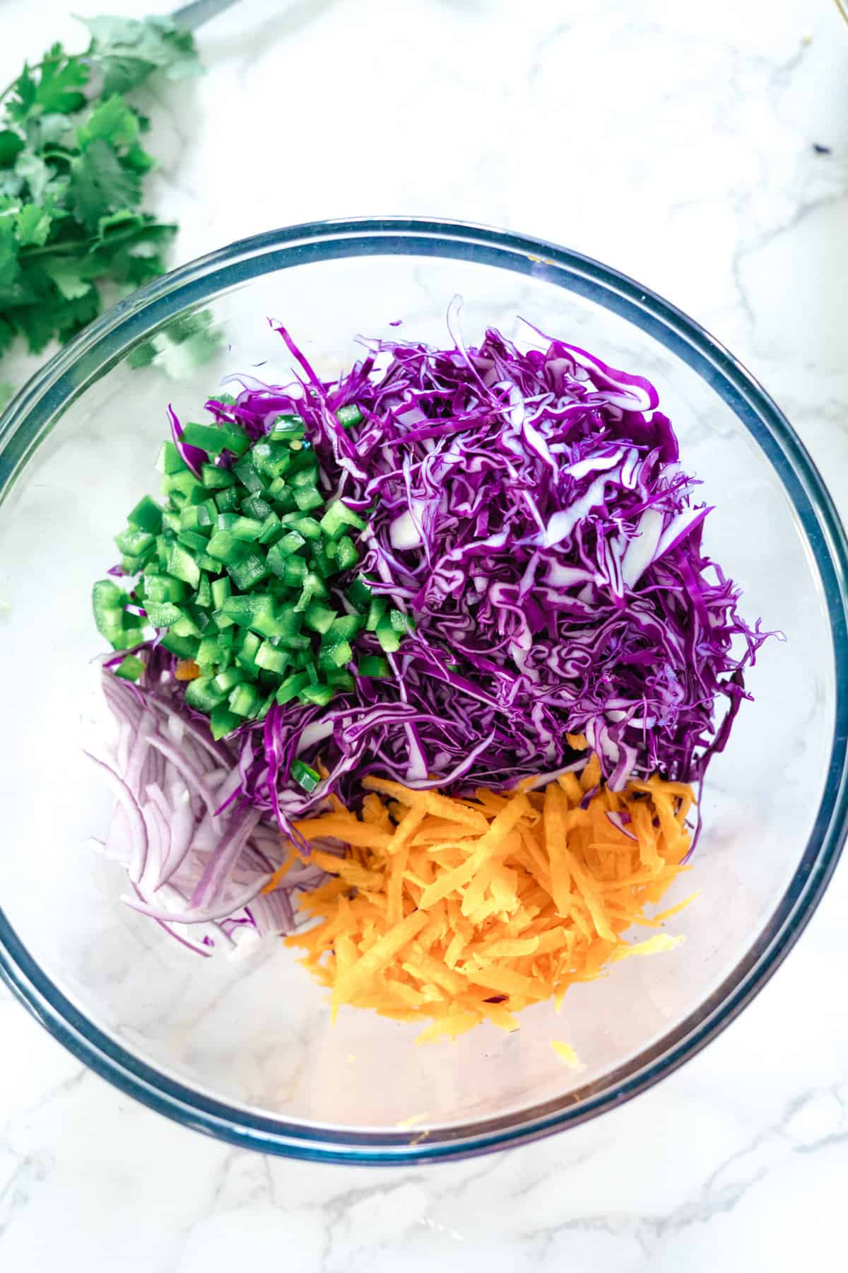 Purple cabbage slaw ingredients in a glass bowl.