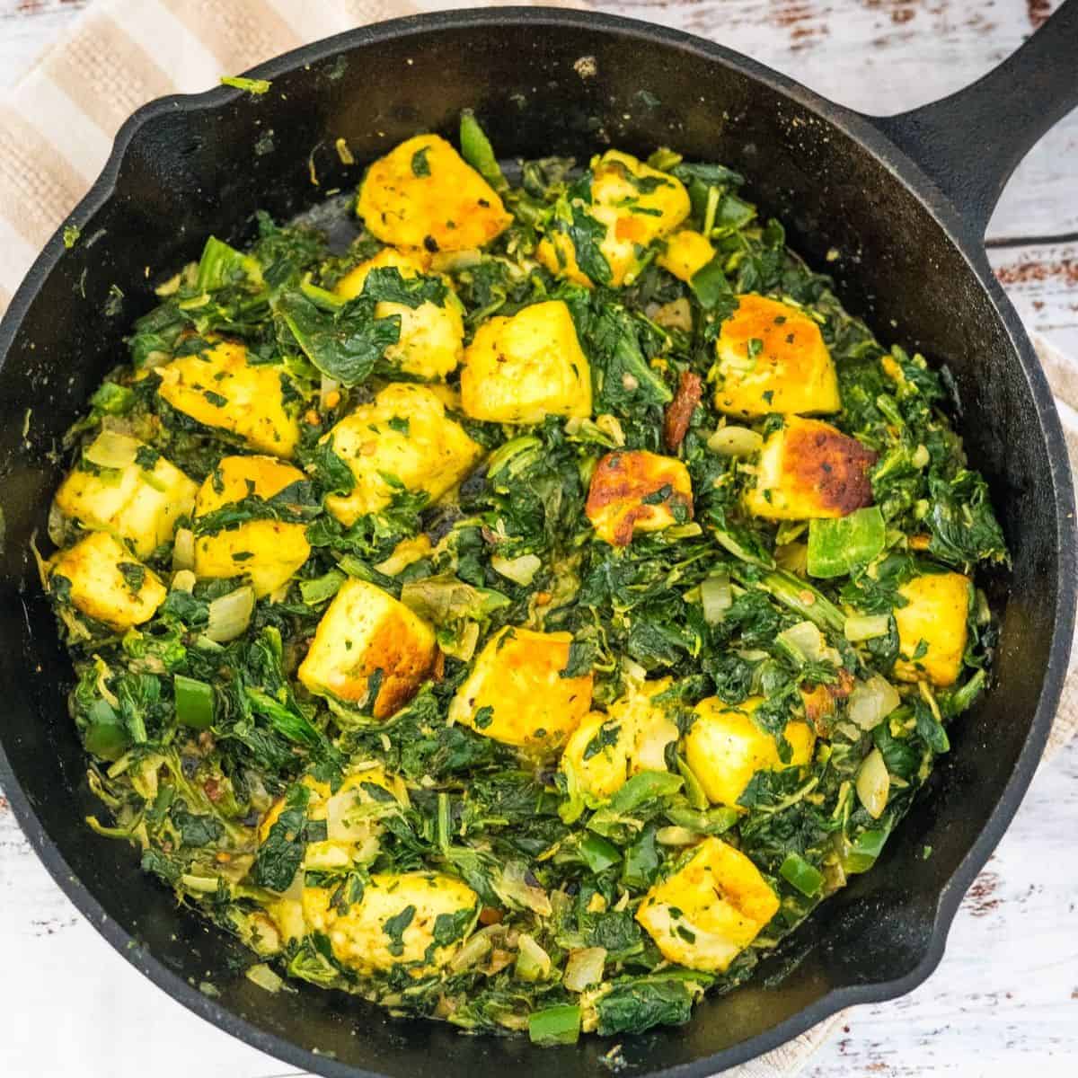 Sautéed paneer and spinach in a cast-iron skillet.