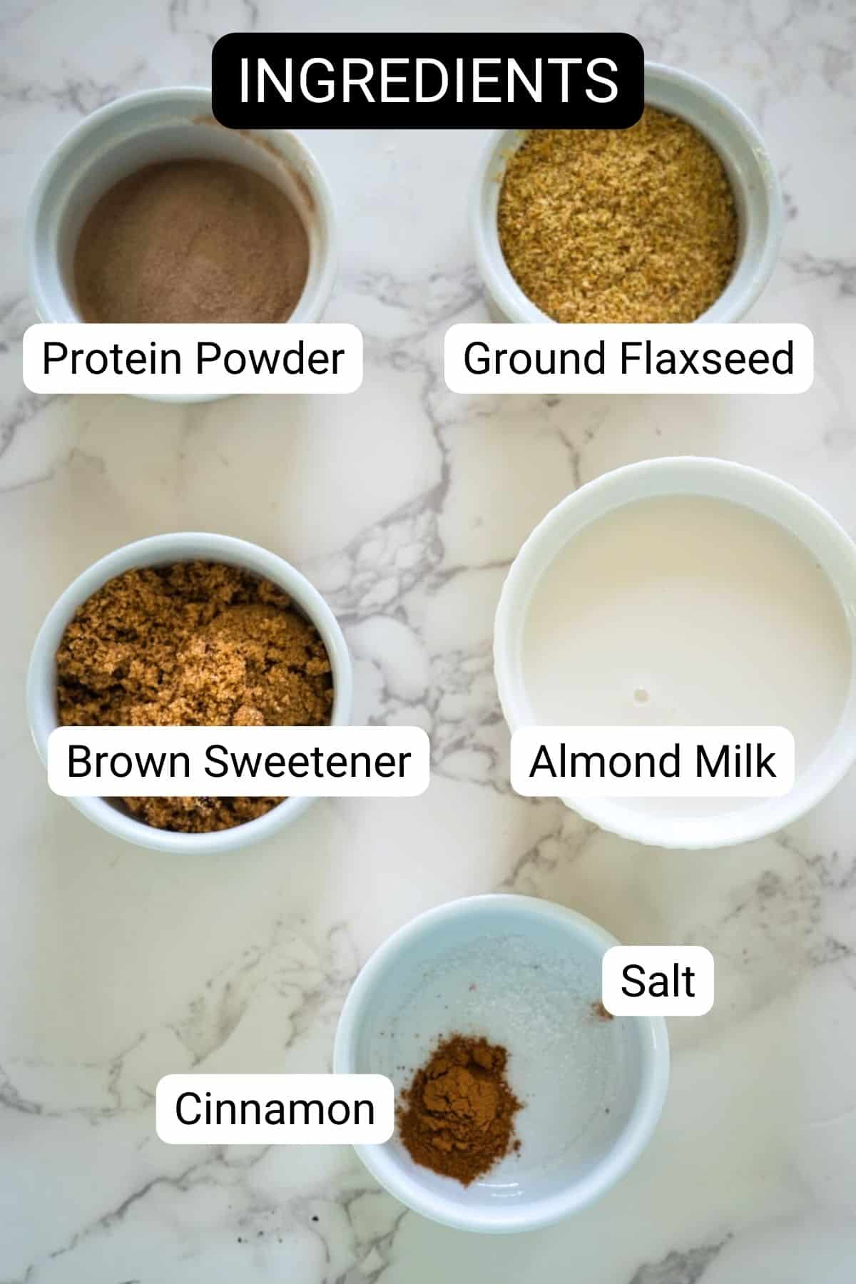 Bowls of various baking ingredients labeled: protein powder, ground flaxseed, brown sweetener, almond milk, salt, and cinnamon.