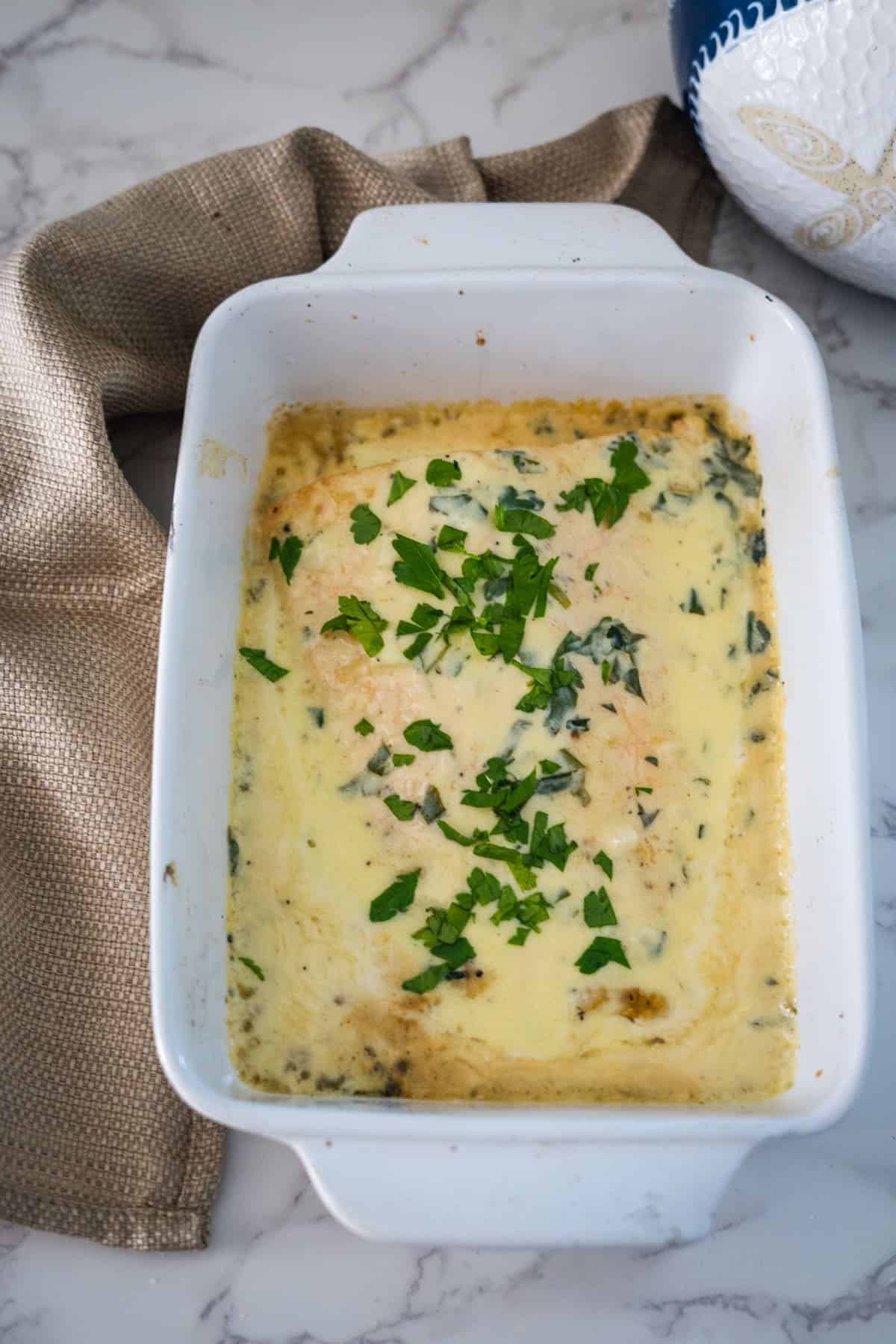 A casserole dish with cheese, spinach, and salmon in lemon creamy sauce in it.