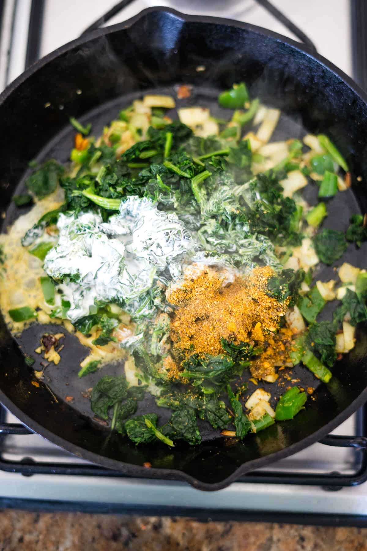 Cooking palak with spices and halloumi in a cast iron skillet on a stove.