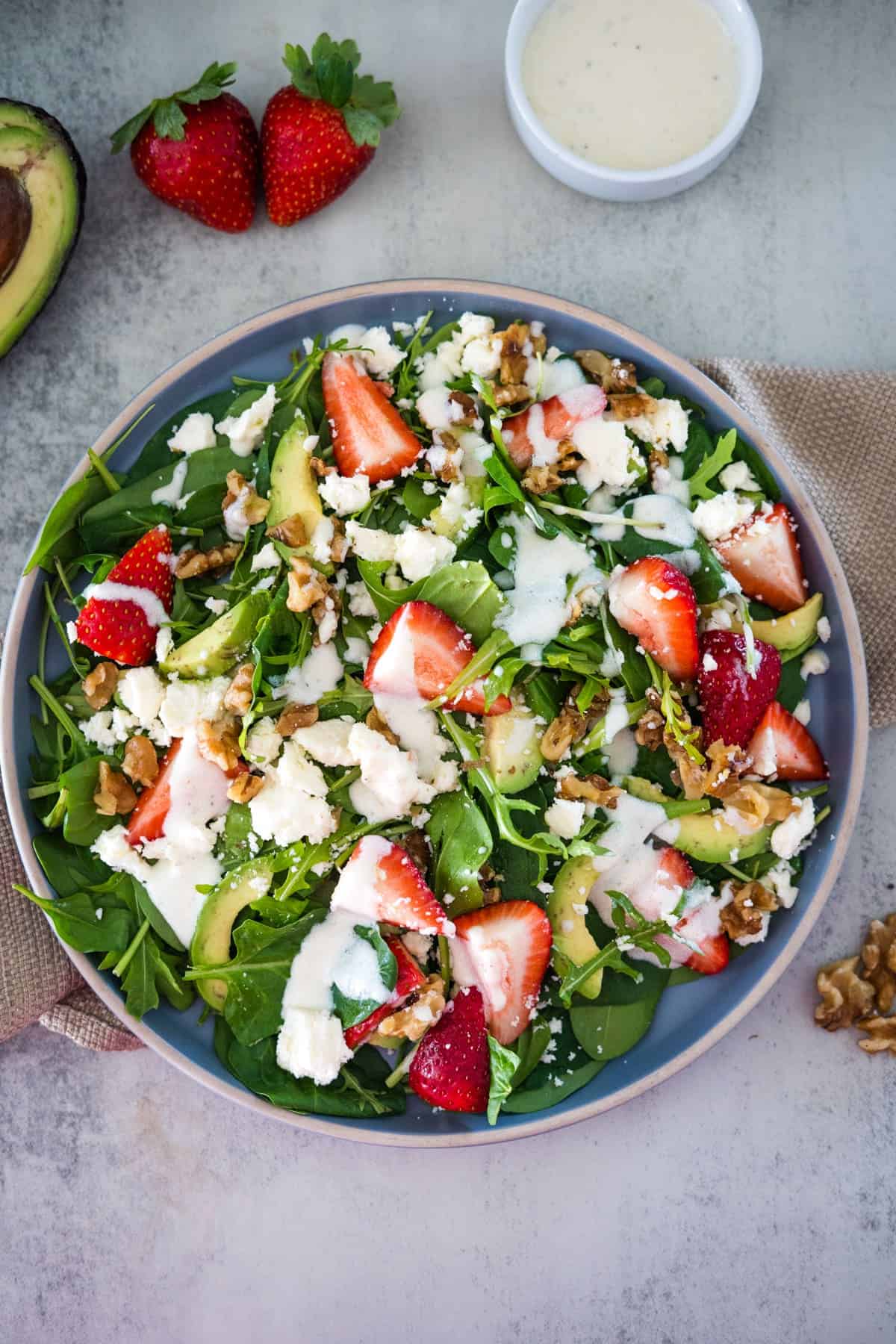 A colorful spinach salad with strawberries, avocado, feta cheese, walnuts, and a creamy dressing served in a bowl.