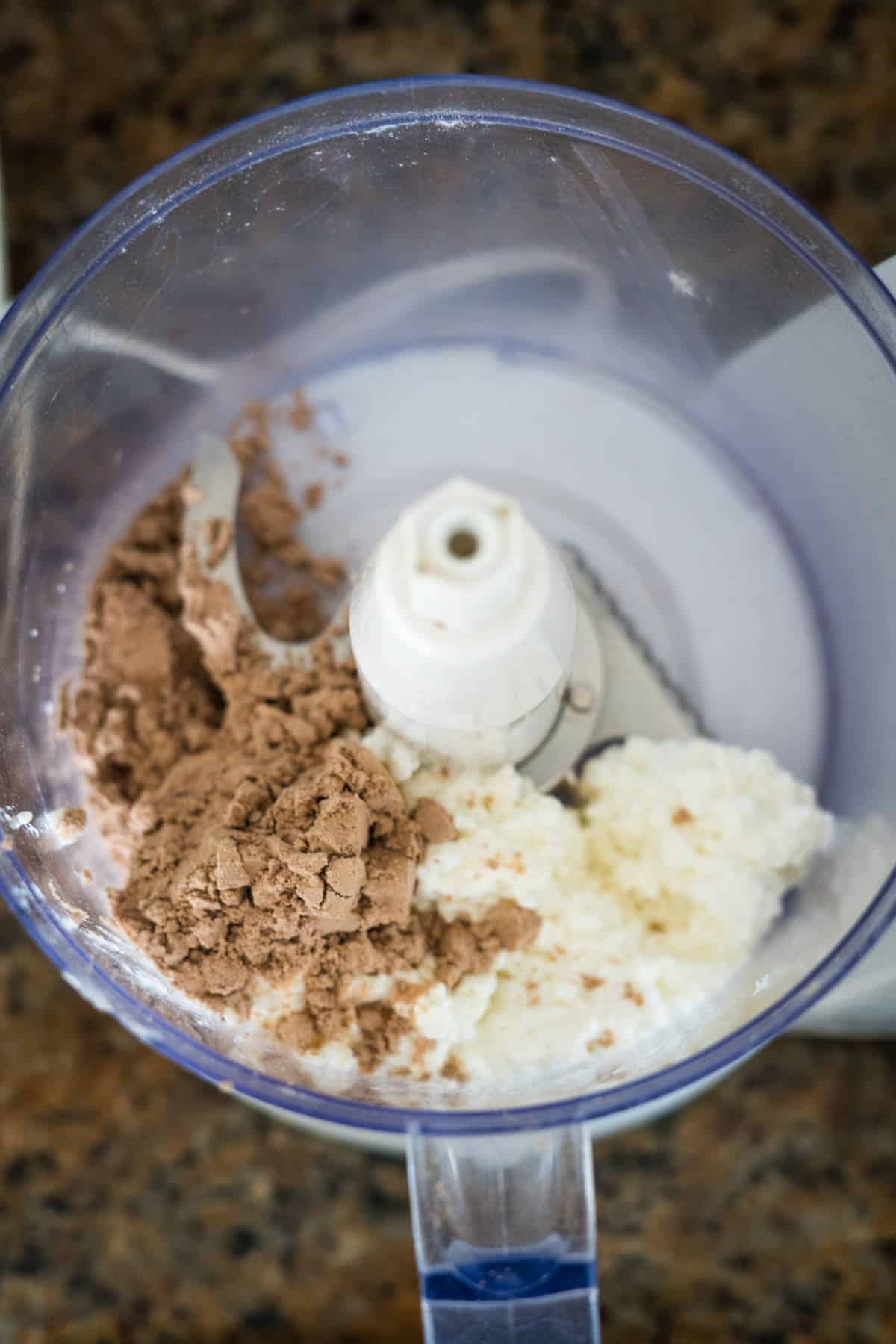 Top view of a blender containing chocolate protein powder and cottage cheese pudding, on a kitchen countertop.